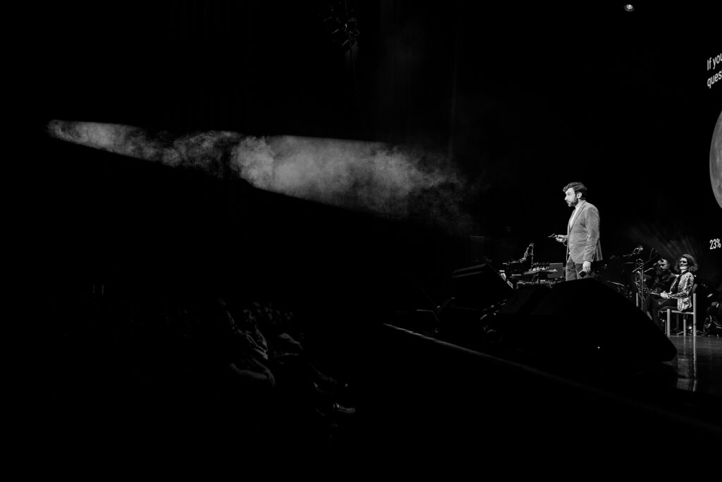 Andrew Steele in the beam of a spotlight while doing science stand-up at the Hammersmith Apollo